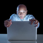 businessman alone at night sitting at computer laptop watching porn or online gambling